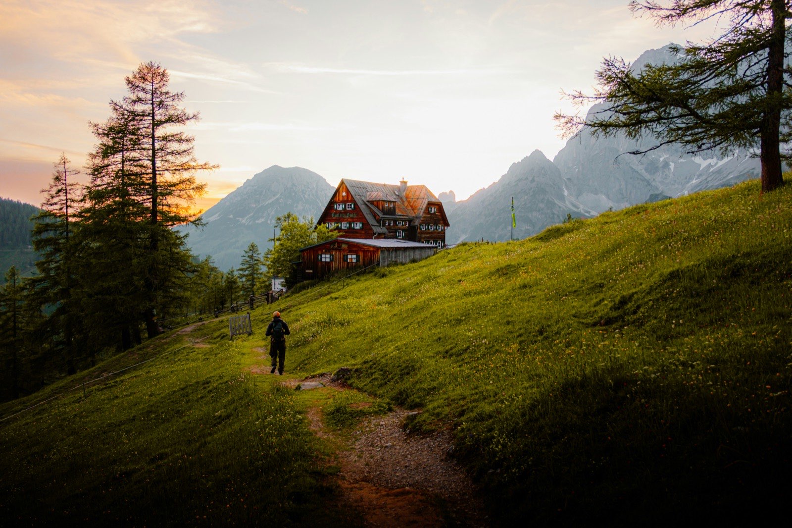 Hiker walking towards a mountain hut at sunset in the Alps
